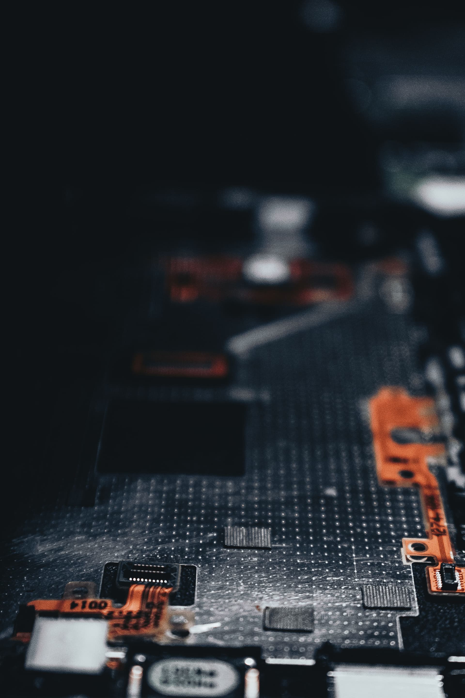 A dark circuit board photographed close up, with orange ribbon connectors in shallow focus.